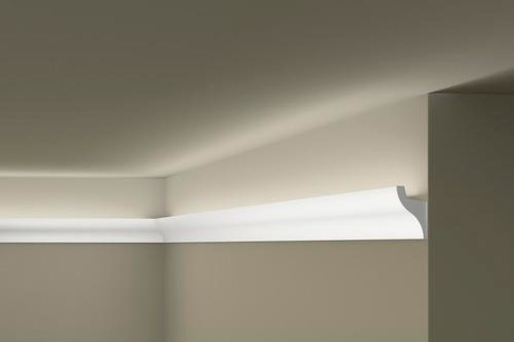 A white decorative molding is installed at the junction of a wall and a ceiling, with subtle lighting highlighting its profile.
