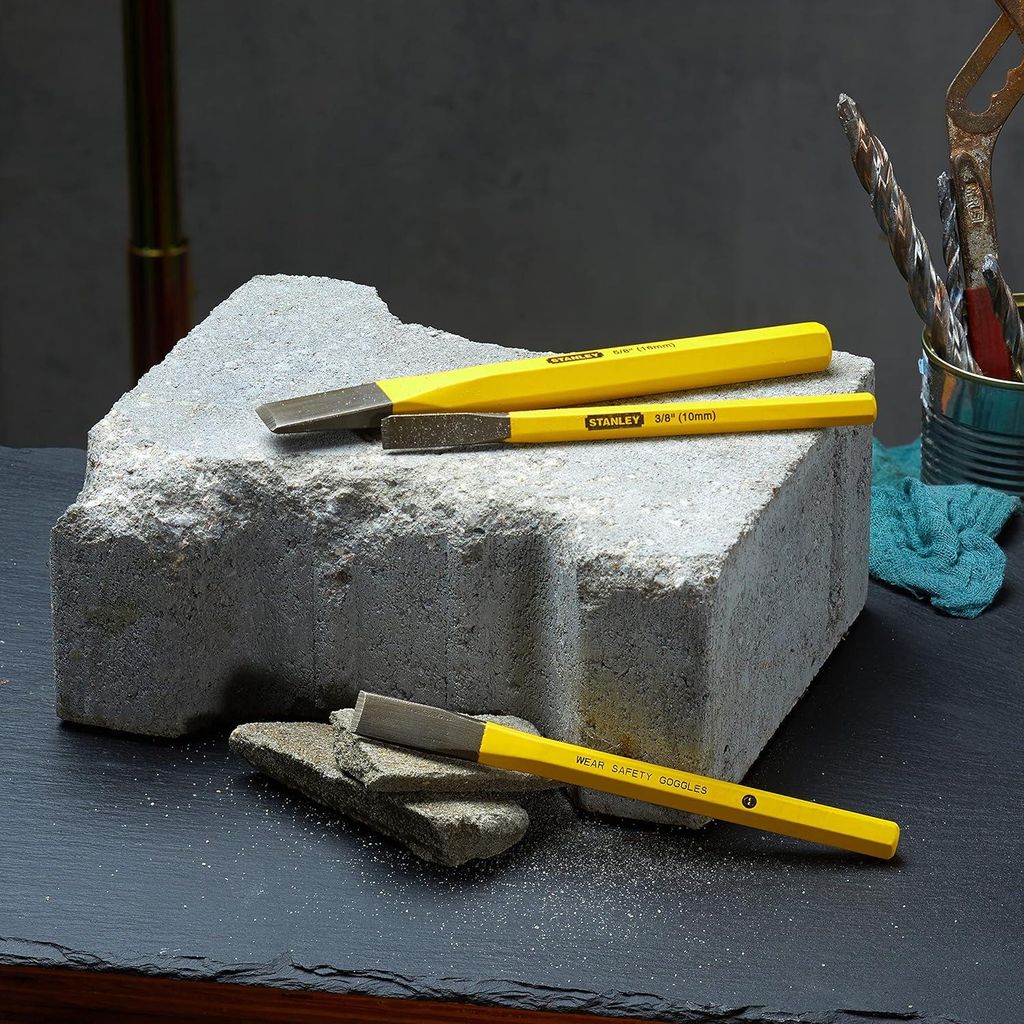 Three yellow chisels are placed on a large gray stone block, with smaller stone fragments in the foreground.