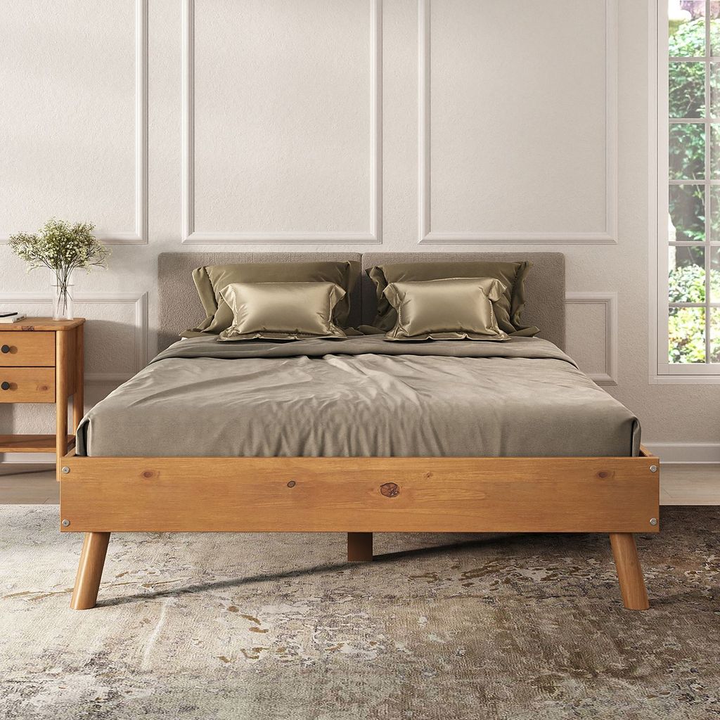 A bed with wooden frame and gray headboard, dressed with bedding and pillows, in a room with decorative wall molding and a window with greenery outside.
