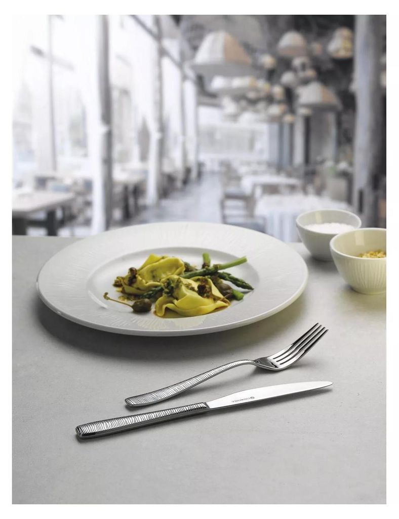 A table setting in a restaurant with a plate of pasta and cutlery.