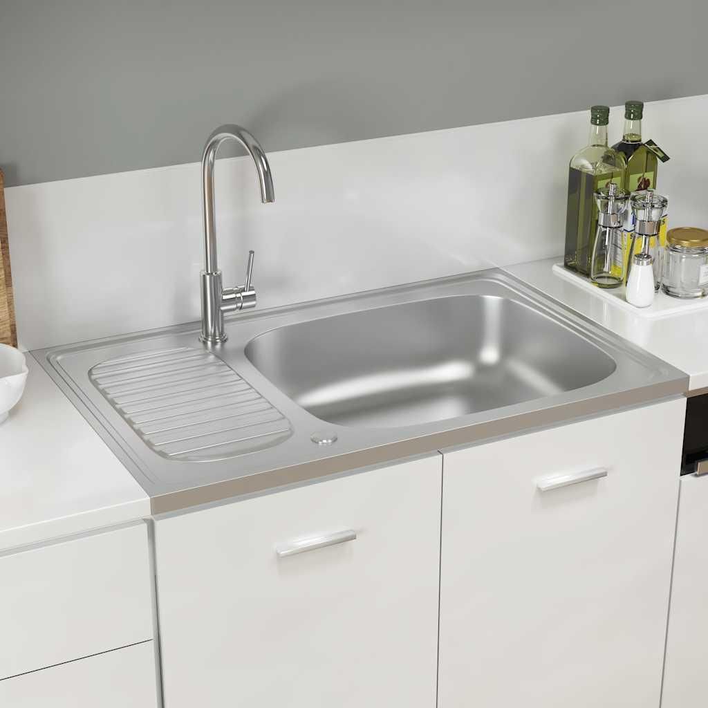 A stainless steel sink with a drainer and faucet, set against a white backsplash and white cabinets.