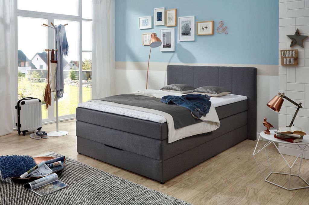 A bedroom scene with a bed, coat rack, suitcase, and decorative items.
