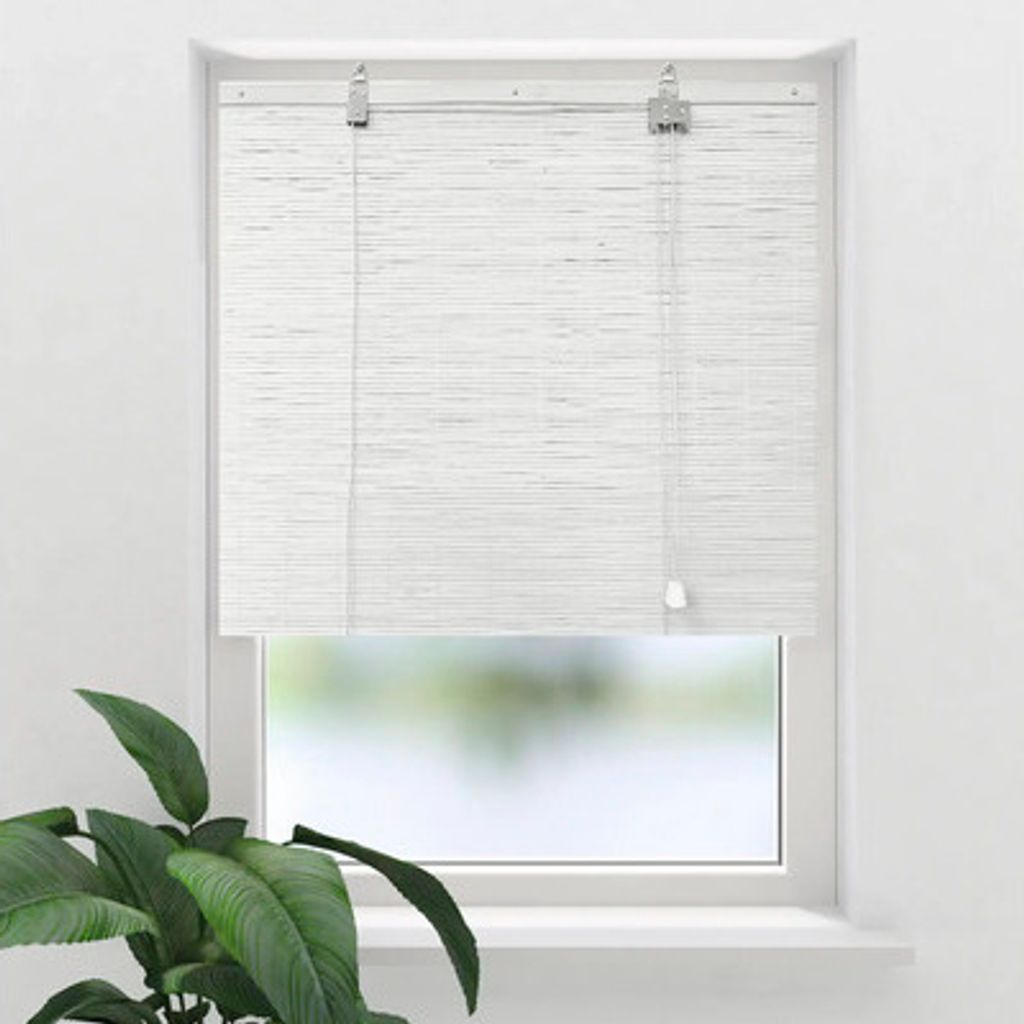 A white bamboo roller blind is shown hanging in a window. A green plant is visible in the foreground.