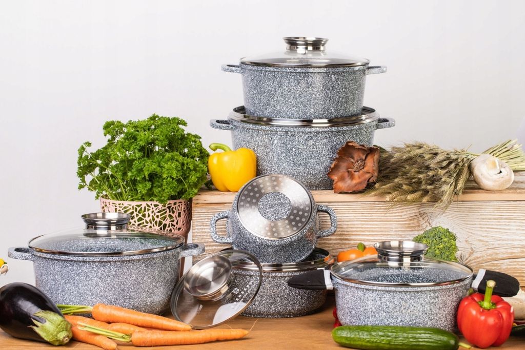 A set of granite-coated pots and pans is displayed with fresh vegetables and herbs.