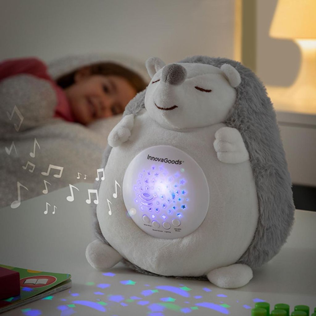 A stuffed hedgehog toy is projecting lights and playing music next to a sleeping child.
