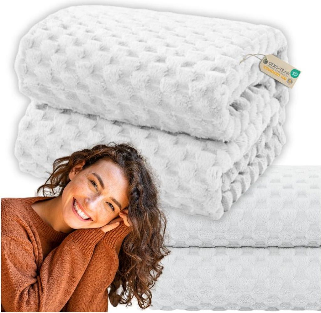 A woman is smiling and leaning on a stack of white blankets.