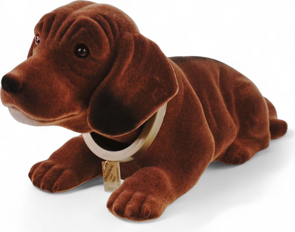 A brown plush dachshund figurine with a collar and tag, lying down on a white background.