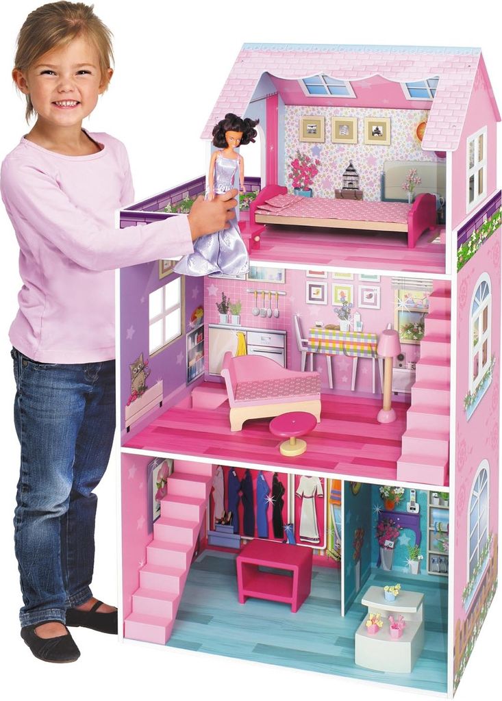A young girl is playing with a large pink dollhouse, holding a doll.