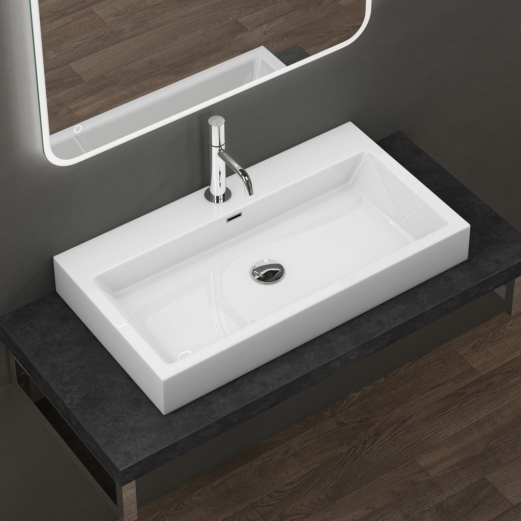 A modern white rectangular basin with a chrome faucet is mounted on a dark countertop, with a large illuminated mirror above it. The background shows a dark gray wall and a wooden floor.