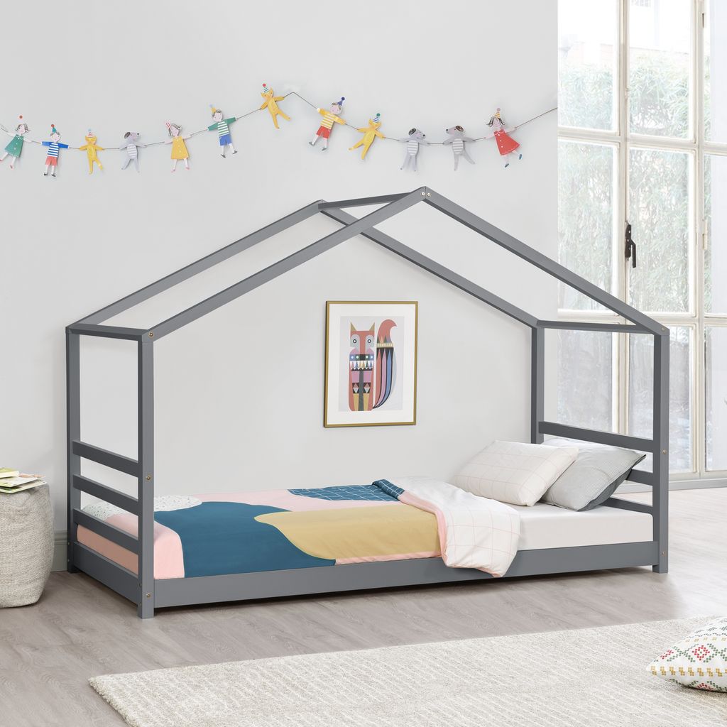 A child's bed with a house-shaped frame, decorated with a string of colorful figures and a framed picture on the wall.
