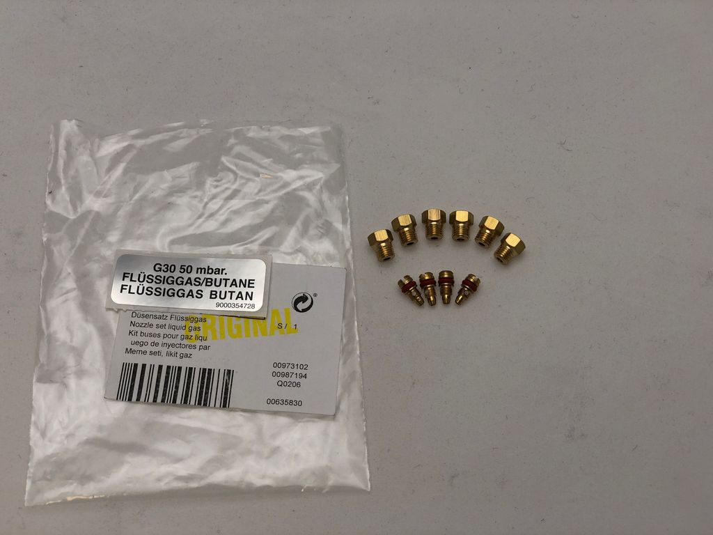 A set of gas nozzles in a plastic bag next to several loose nozzles on a light gray surface.
