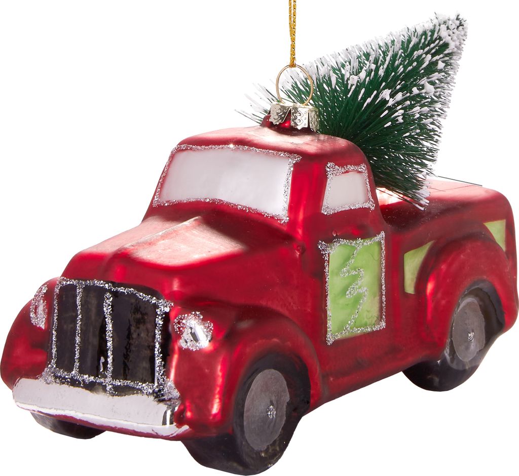 A close-up studio shot of a red glass Christmas ornament shaped like a pickup truck with a small green Christmas tree in the bed.