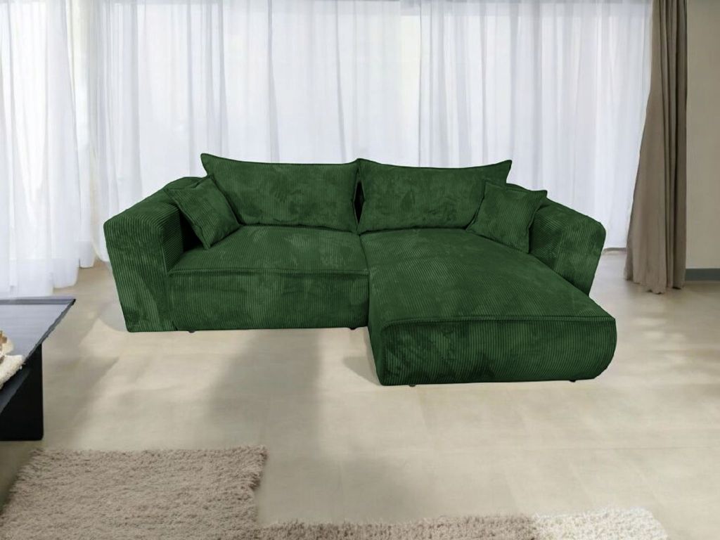 A green sectional sofa is shown in a room with sheer white curtains in the background and a rug on the floor.
