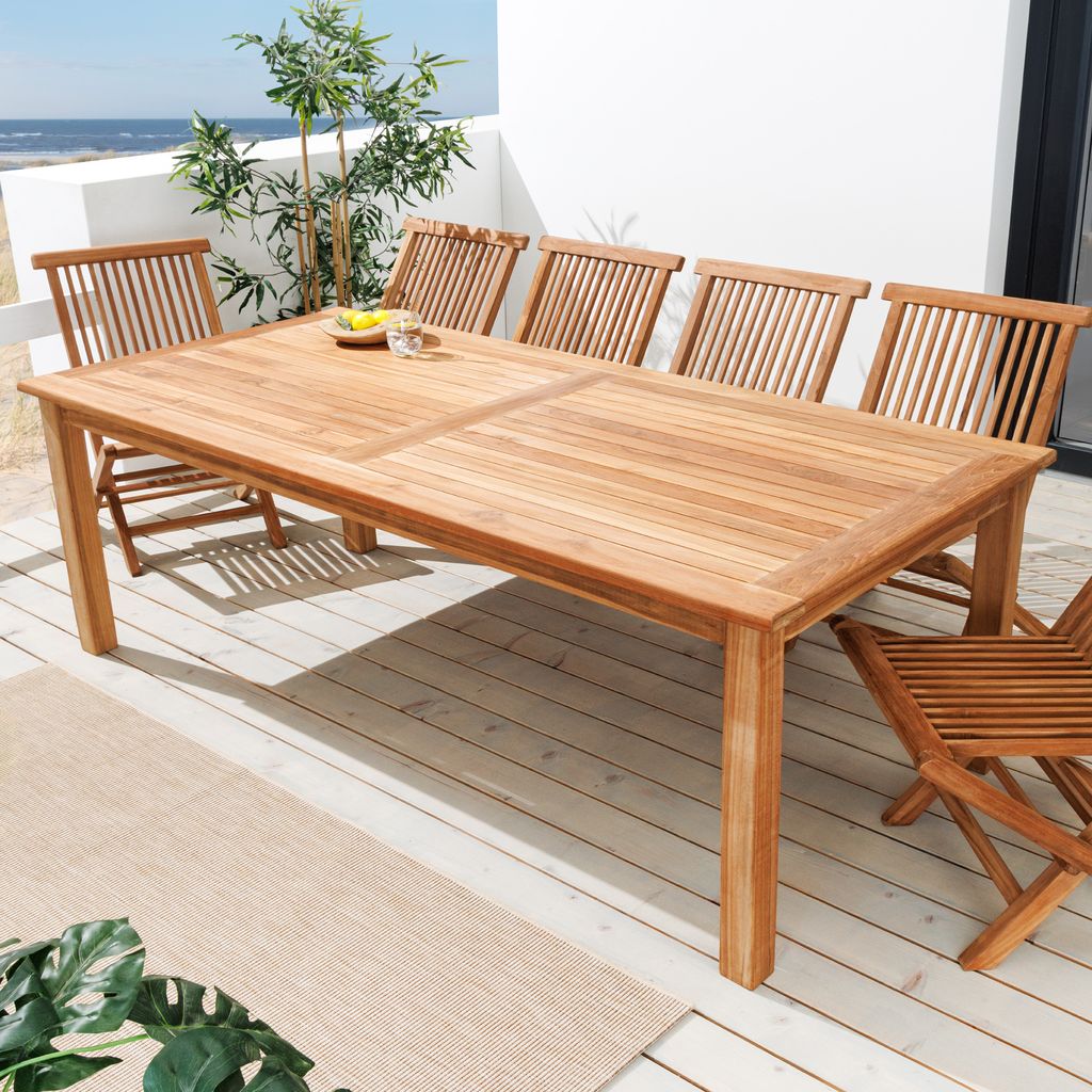 A teak dining set on a wooden deck with a view of the ocean.