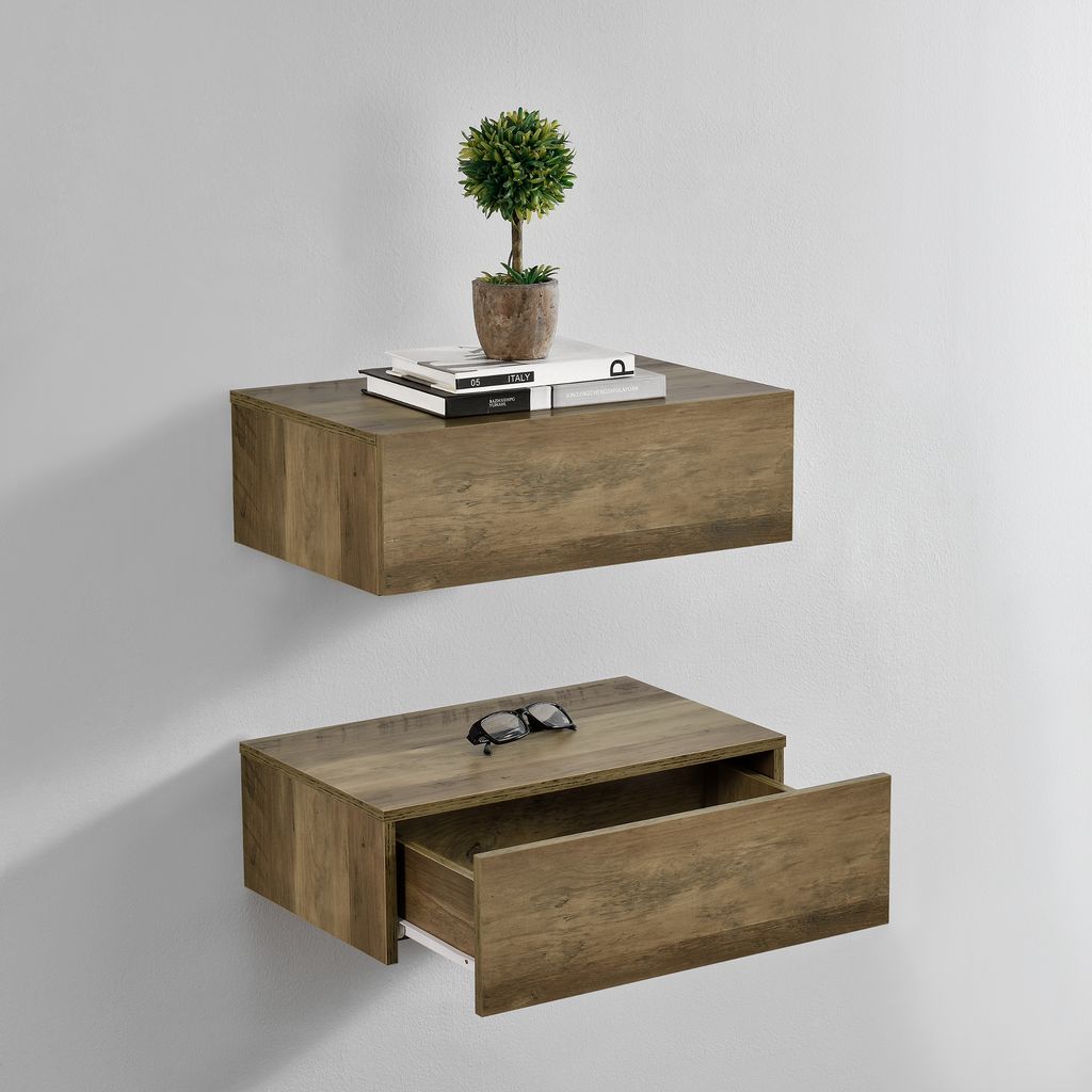 Two wooden floating shelves mounted on a light gray wall. The top shelf has books and a small potted plant. The bottom shelf has a pair of sunglasses and an open drawer.