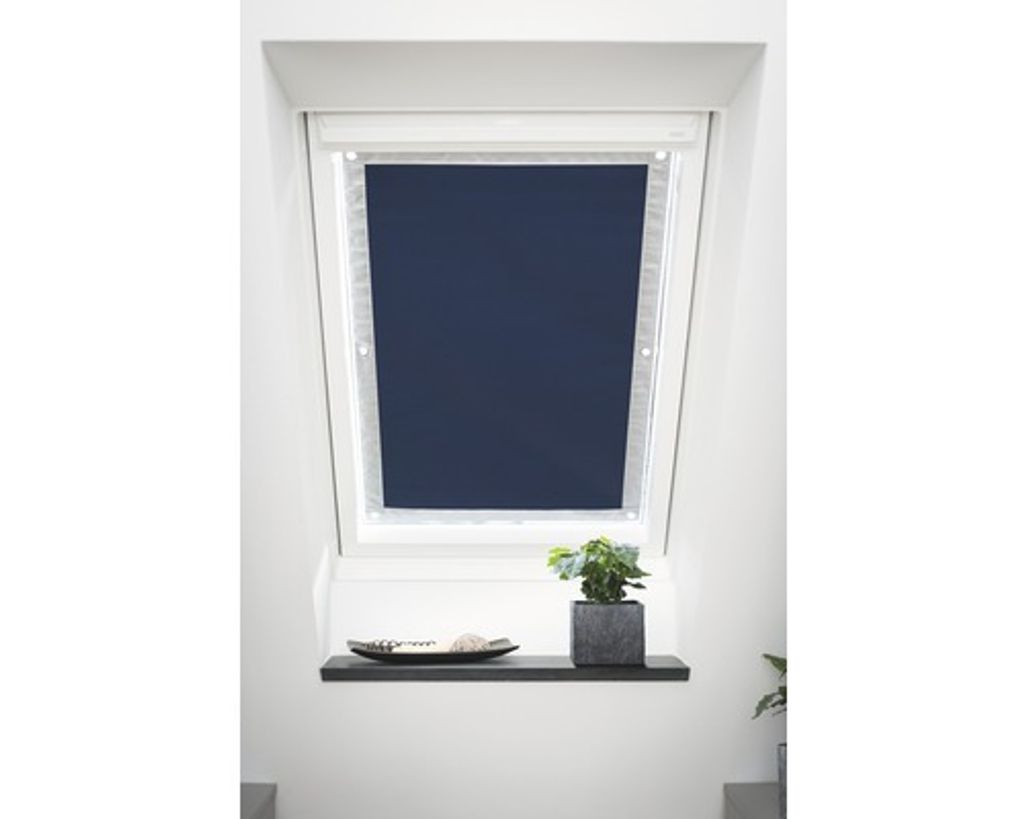 A dark blue roller blind is installed in a slanted window, with a small plant and a decorative bowl on a shelf below.