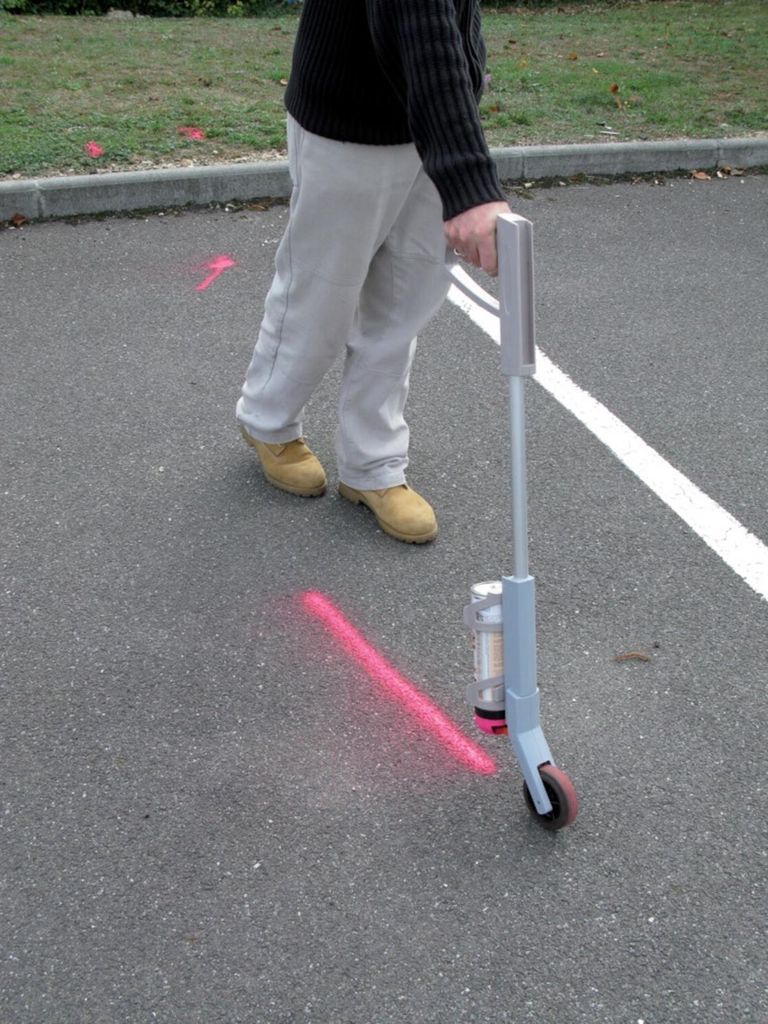 A person is using a marking stick on an asphalt surface with pink spray paint marks.
