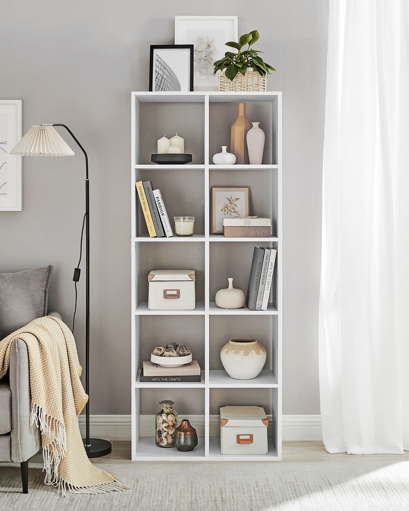 A white shelving unit filled with decorative items, books, and storage boxes, next to a sofa and a floor lamp.