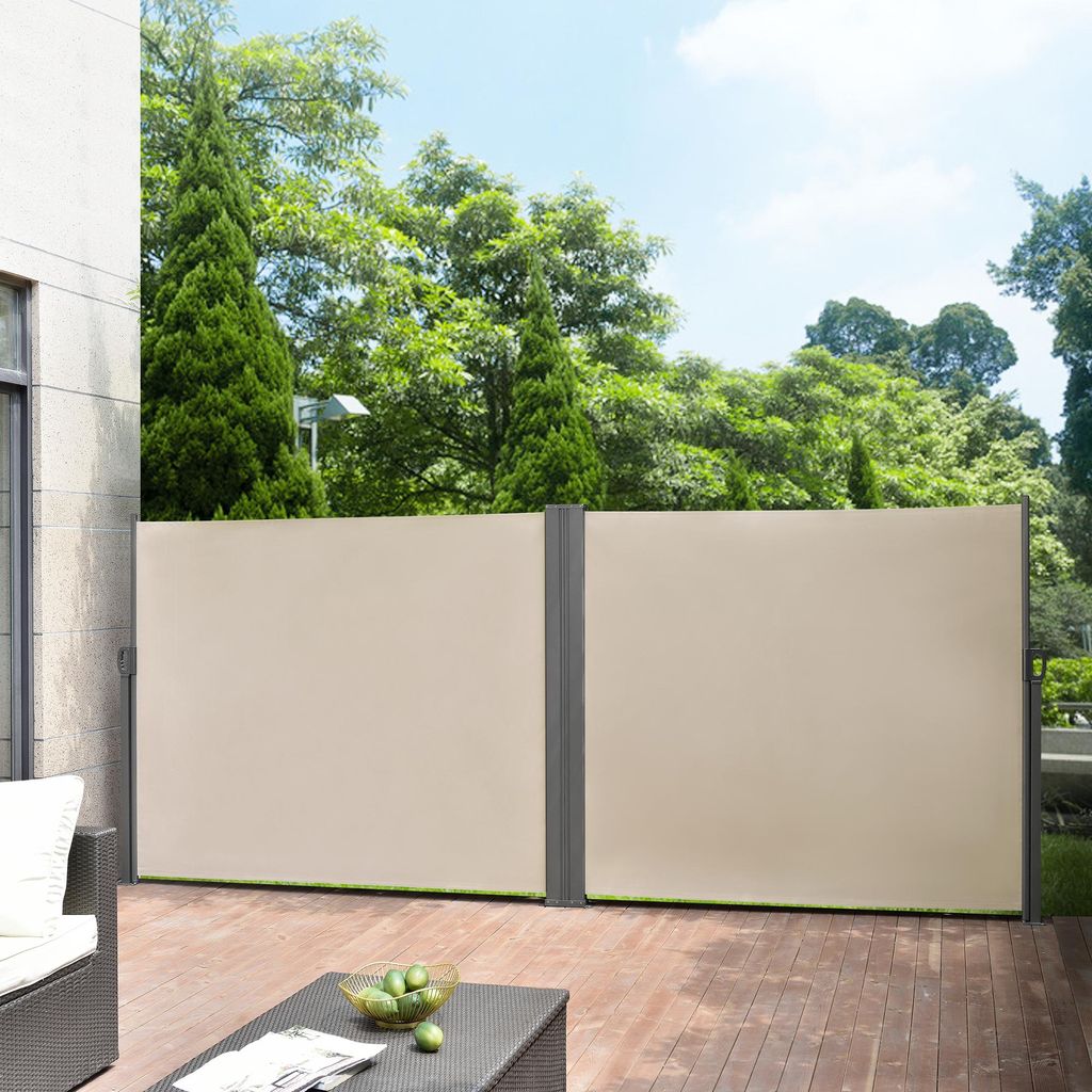A patio with wooden decking and two beige retractable side awnings, with trees and a blue sky in the background.