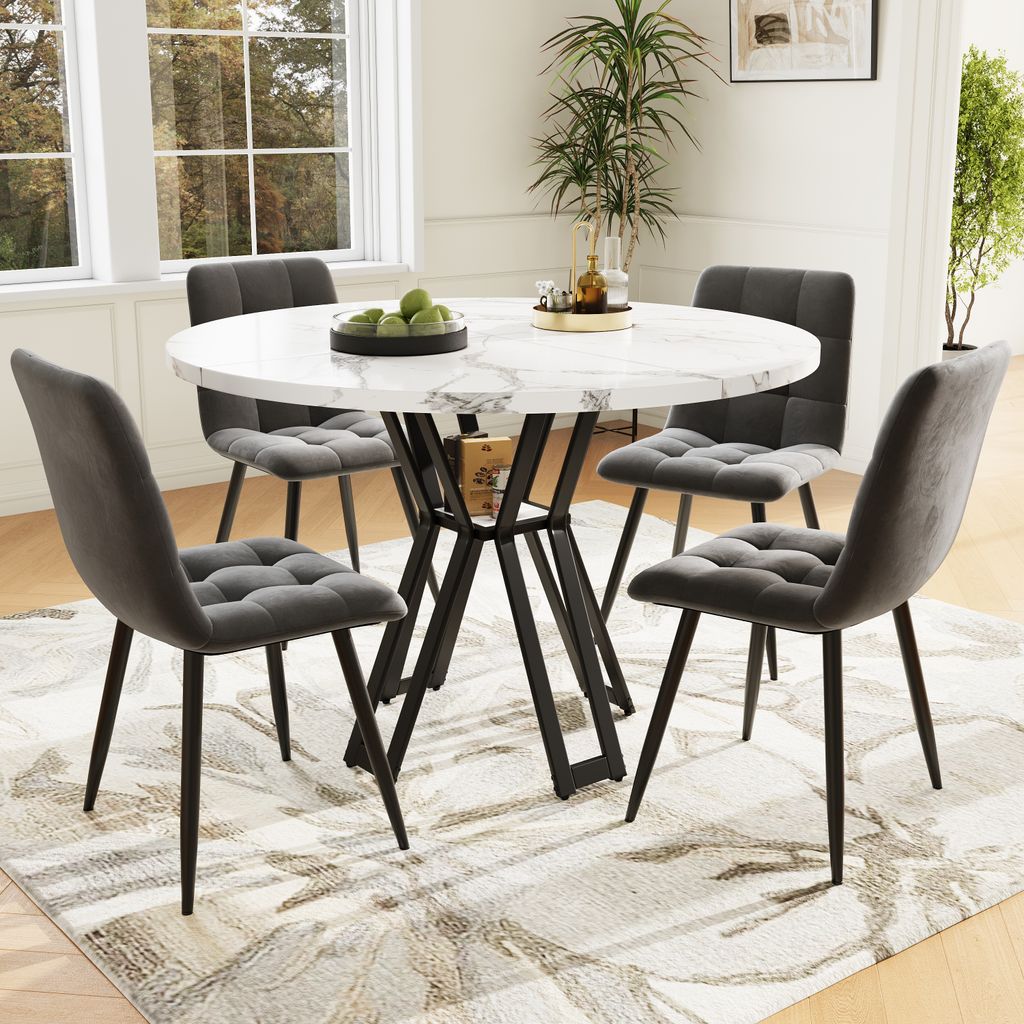 A dining set with a round marble-top table and four gray upholstered chairs, placed on a patterned rug in a well-lit room with windows.