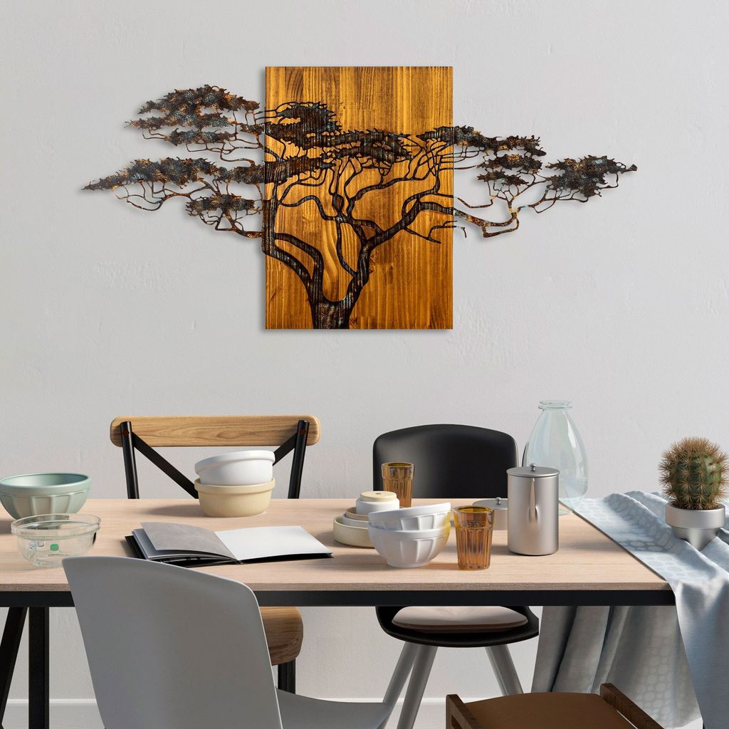 A dining table set with bowls, glasses, and a cactus, with a metal tree wall art hanging above it.