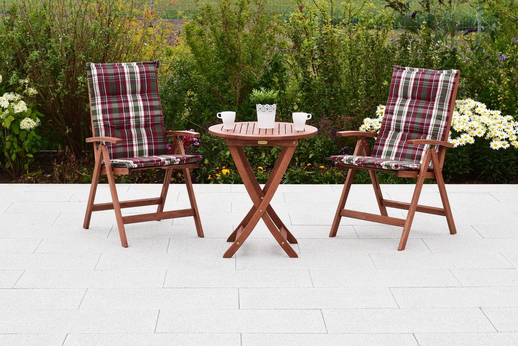 A wooden garden furniture set with two chairs and a table on a paved patio, surrounded by greenery.