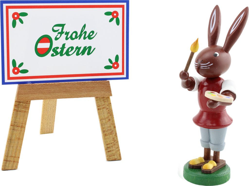 Ein fröhlicher Osterhase mit Pinsel und Palette steht neben einem Schild mit der Aufschrift Frohe Ostern das auf einer Staffelei präsentiert wird