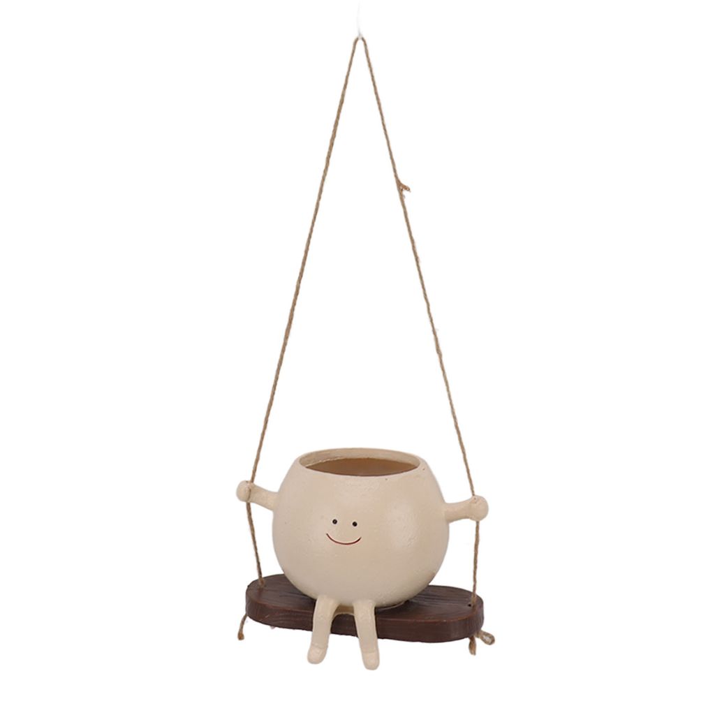 A hanging planter shaped like a round character with a smiley face, sitting on a swing.