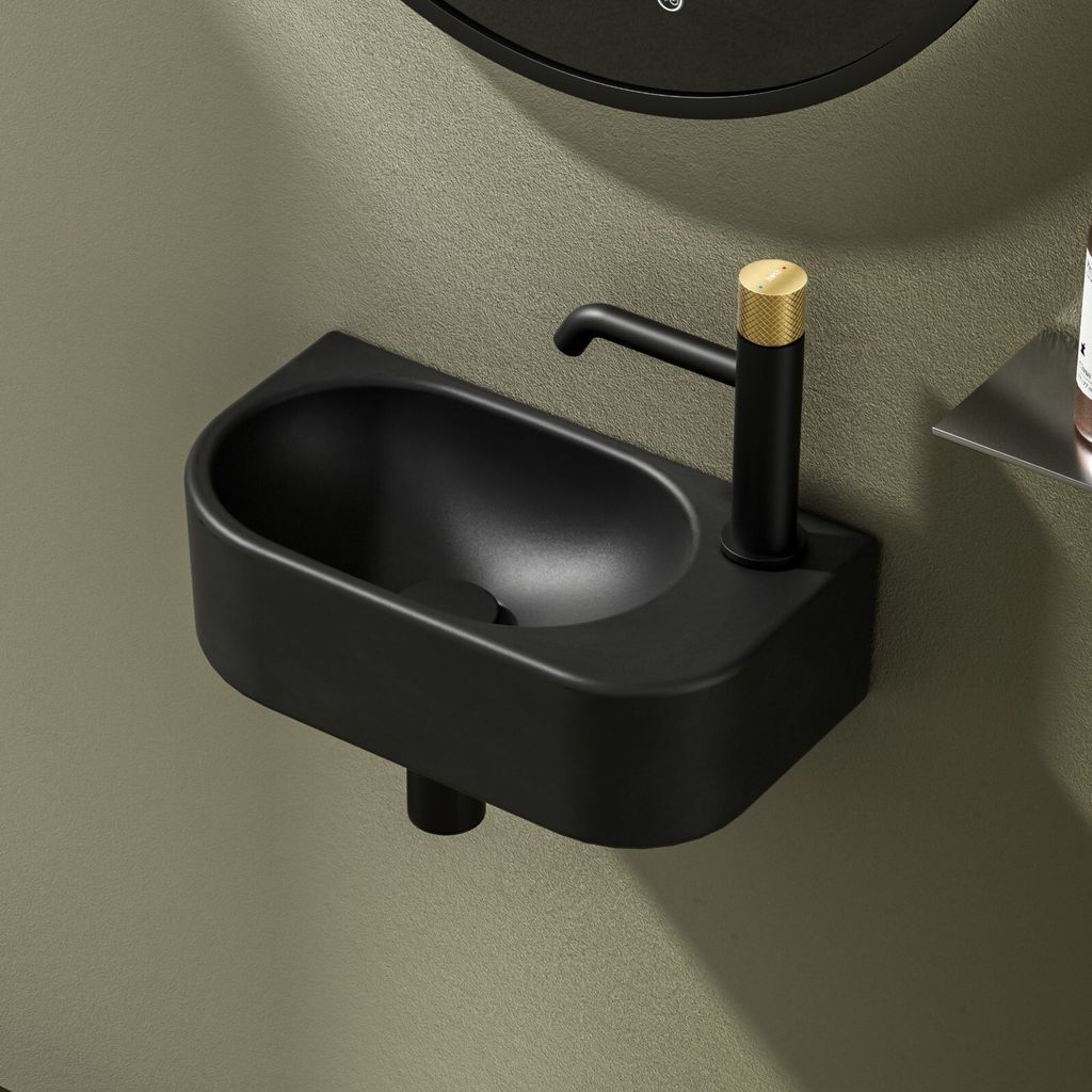 A close-up shot of a black ceramic corner wall-mounted sink with a black faucet with a gold accent.