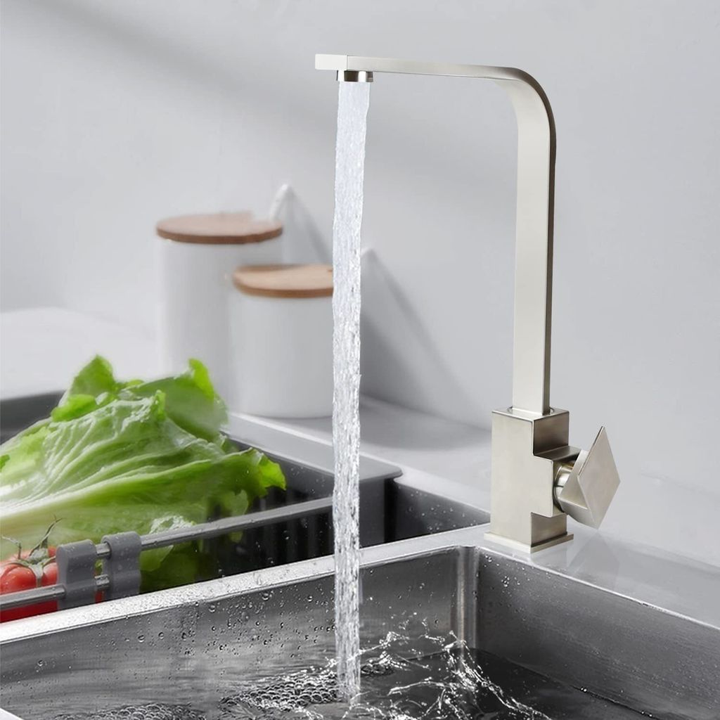 A kitchen faucet with water running into a sink, with lettuce and tomatoes in the sink.