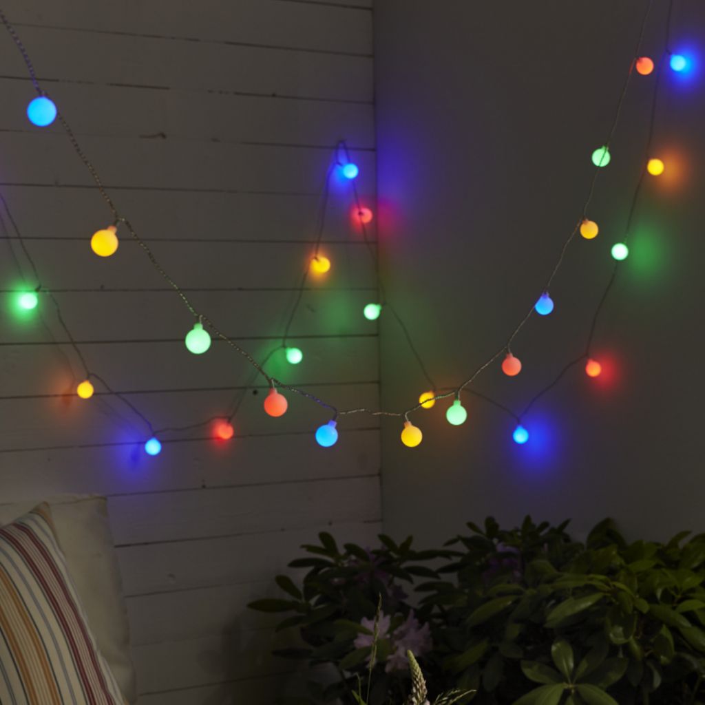 A string of colorful LED party lights is draped along a wooden wall and a darker wall, with some greenery visible at the bottom.