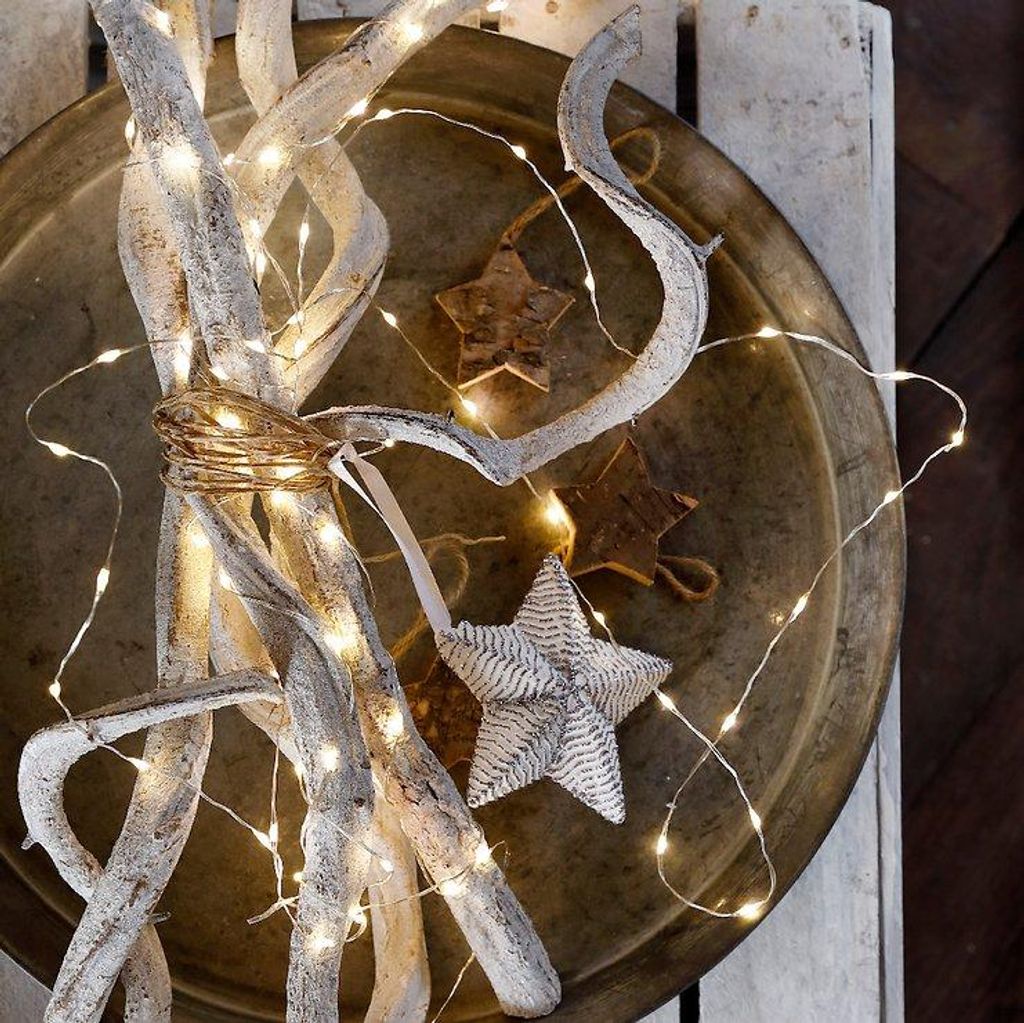 A decorative arrangement of white branches with fairy lights and star ornaments on a rustic tray.