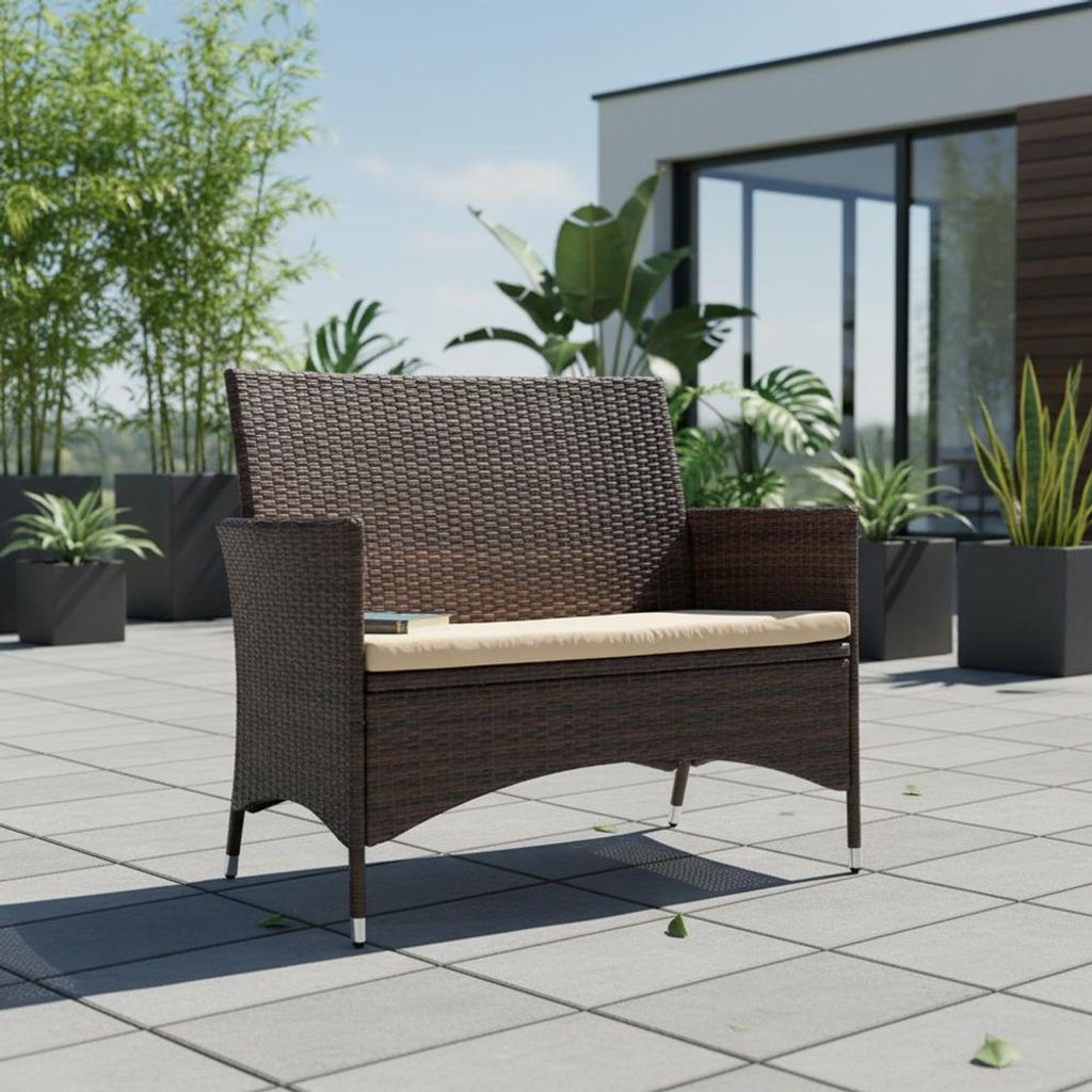 A brown rattan bench with a beige cushion sits on a tiled patio, surrounded by potted plants and a modern building.