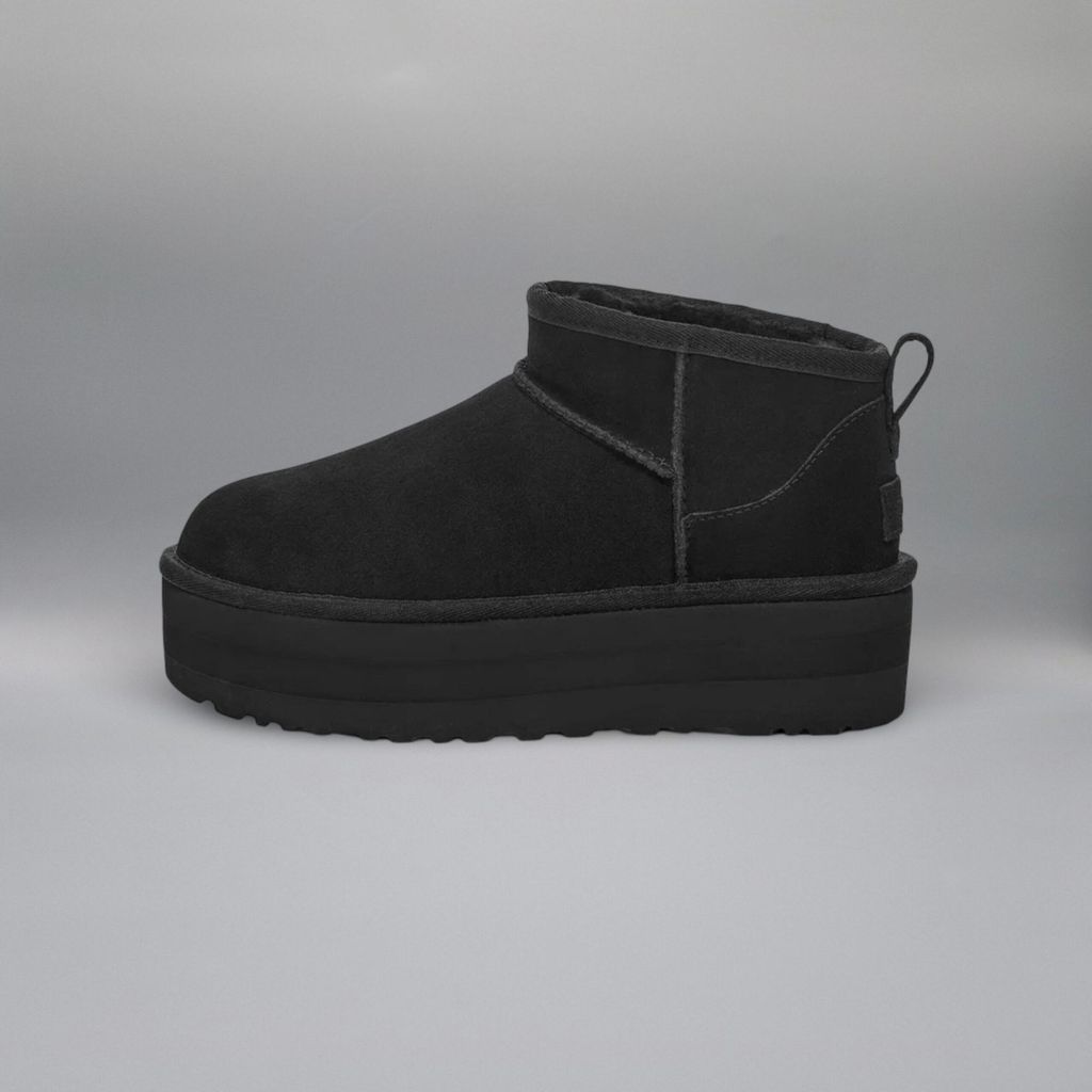 A black UGG boot with a platform sole is shown against a plain gray background.