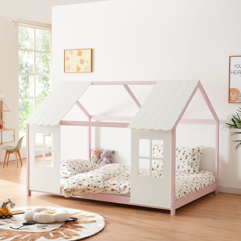 A child's bed with a house-shaped frame, decorated with stuffed animals and bedding, in a room with a window and artwork on the wall.