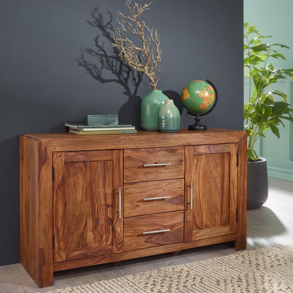 A wooden sideboard with decorative items on top, including vases, a globe, and a plant in the background.