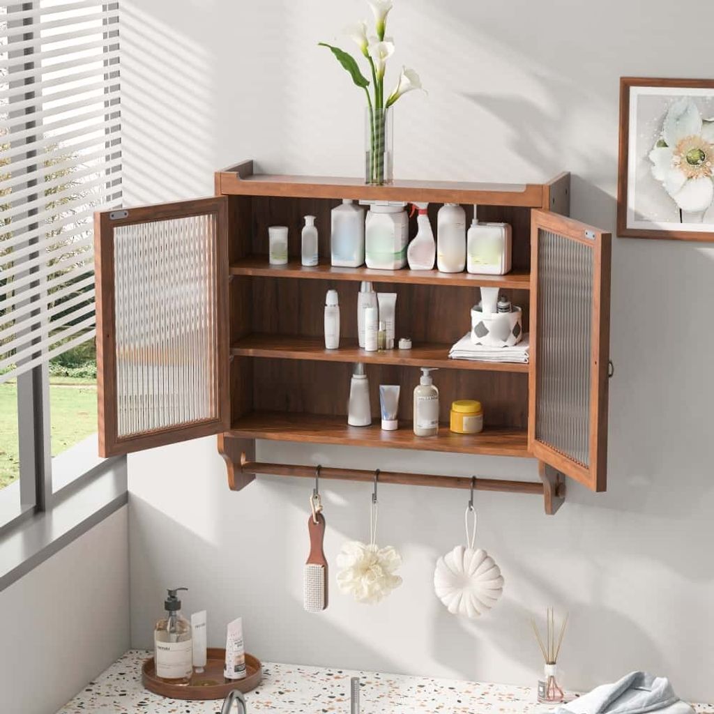 A wooden wall-mounted cabinet with glass doors, filled with various bathroom products, is shown in a well-lit room with a window.