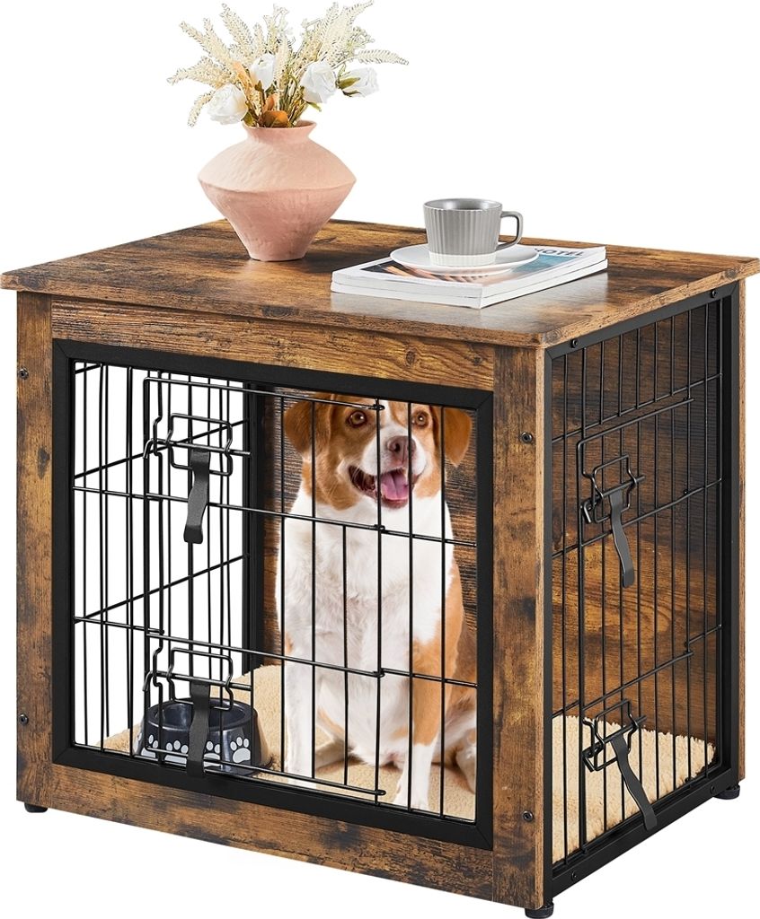 A dog is sitting inside a wooden dog crate that is designed to look like a side table. There is a vase with flowers and a cup on top of the crate.