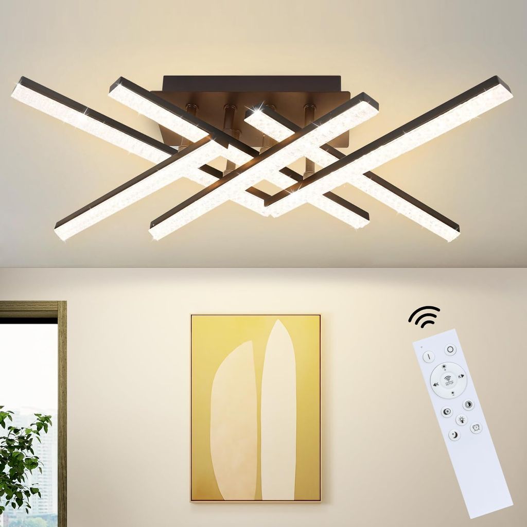 A modern LED ceiling light fixture with multiple intersecting arms, illuminated and mounted on a white ceiling. A remote control is shown in the lower right corner, and a framed abstract painting hangs on the wall below.
