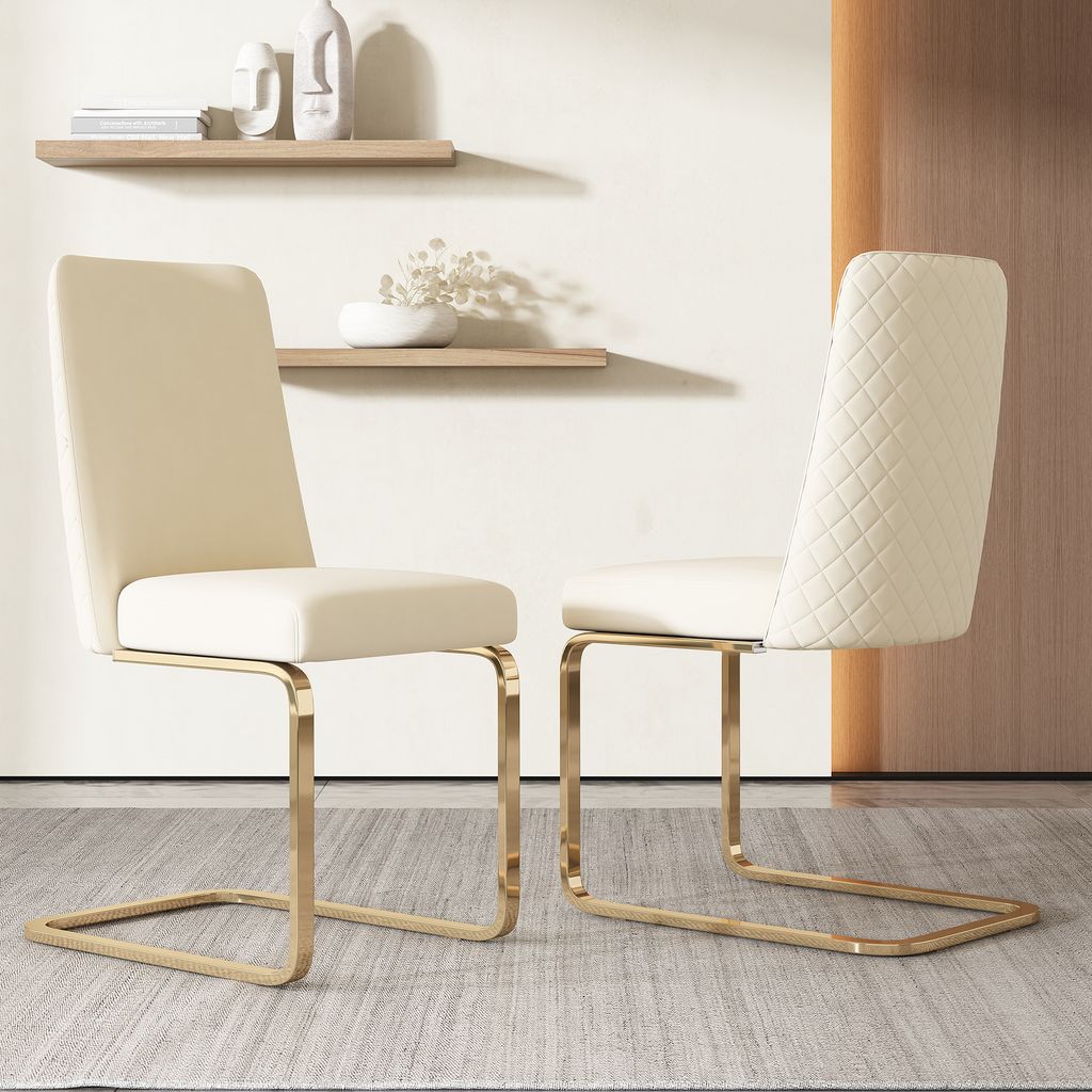 Two beige dining chairs with gold metal legs are shown in a room with shelves on the wall.