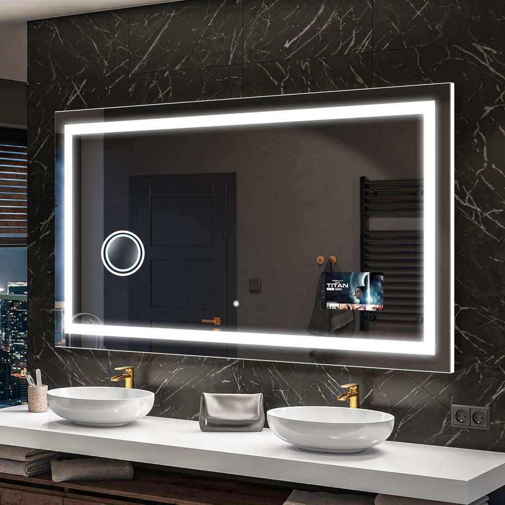 A modern bathroom vanity with a large illuminated mirror, two sinks, and gold faucets.