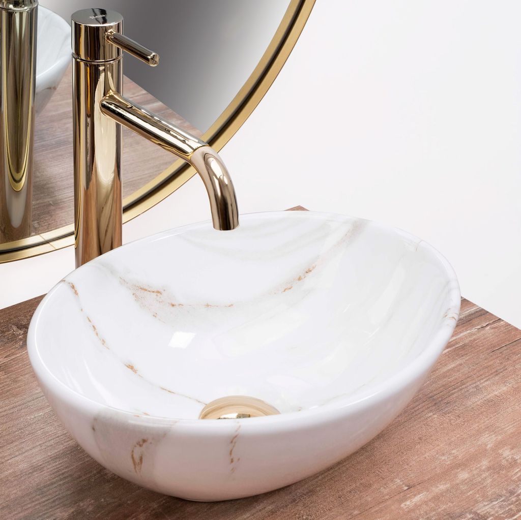 A close-up view of a marble-patterned vessel sink with a gold faucet, placed on a wooden surface.
