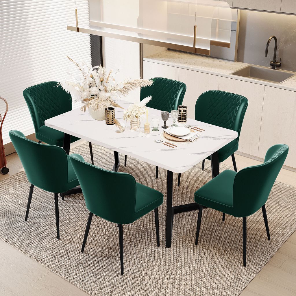 A dining set with a marble-top table and six green velvet chairs in a modern kitchen setting.