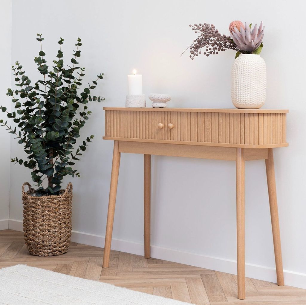 A console table with decorative items and a plant in a basket.