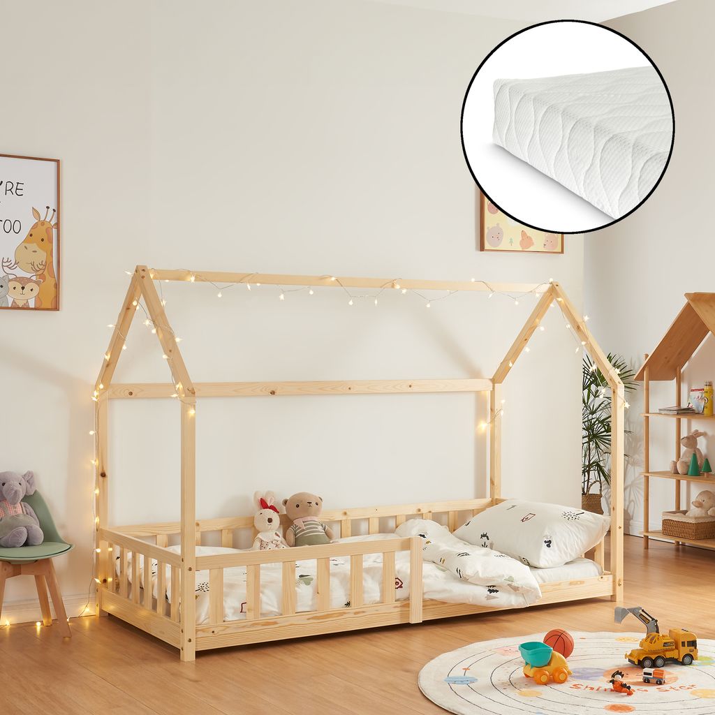 A children's house bed with a mattress and fairy lights in a room.