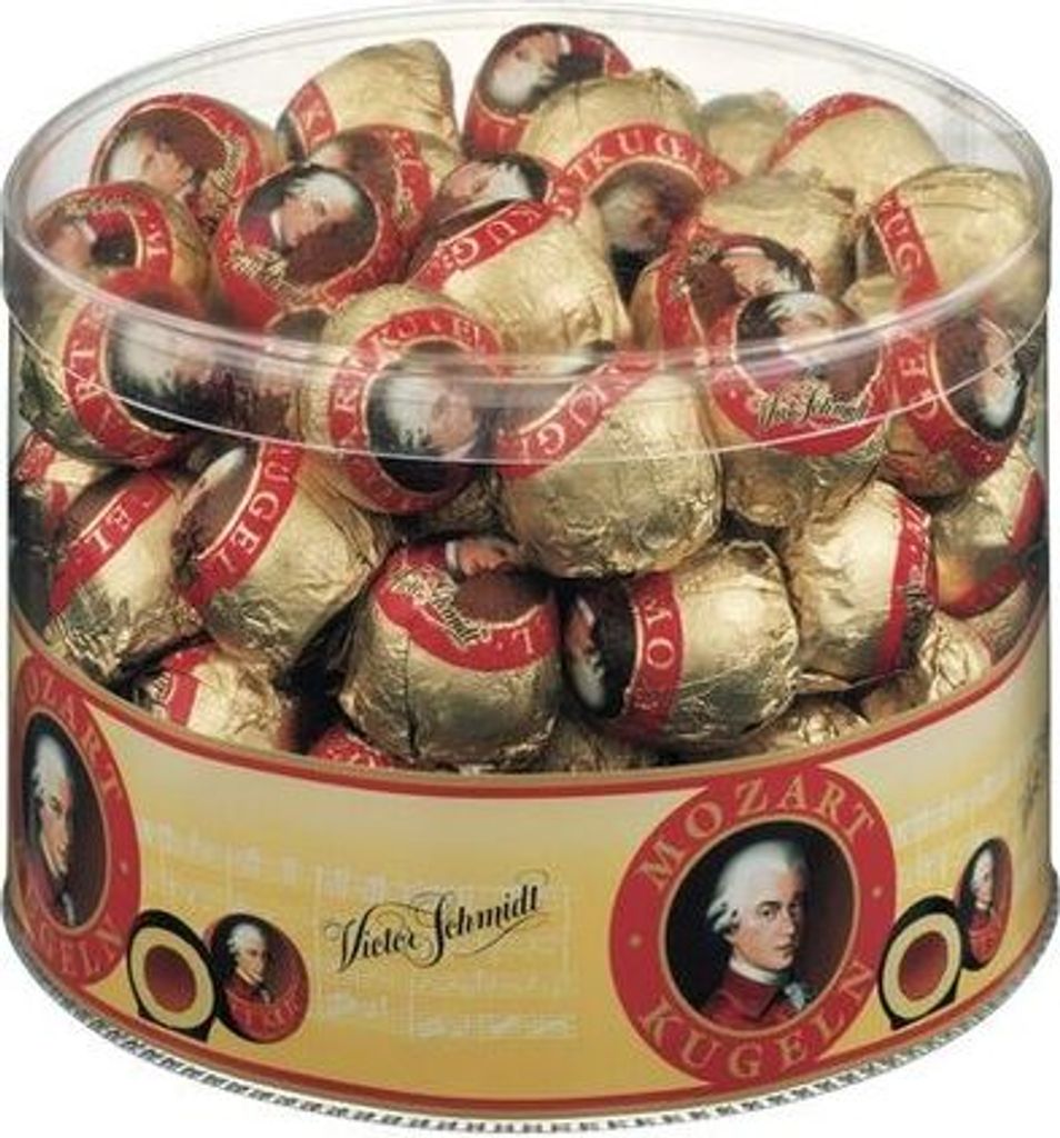 A clear plastic container filled with individually wrapped Mozartkugeln chocolates. The container has a decorative label with images of Mozart and text.