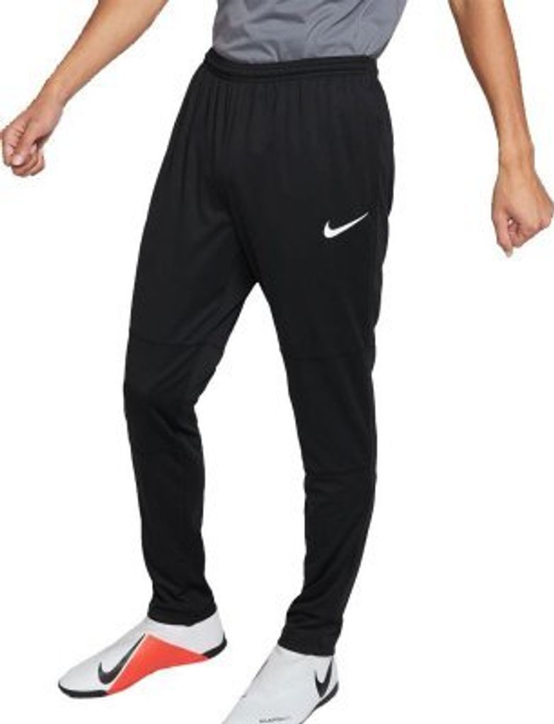 A person wearing black Nike sport trousers and white and orange athletic shoes.