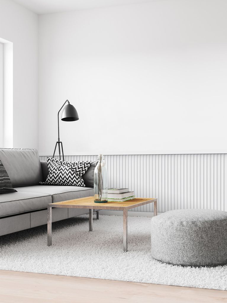 A minimalist living room scene with a gray sofa, a coffee table, a floor lamp, and a fluffy ottoman.