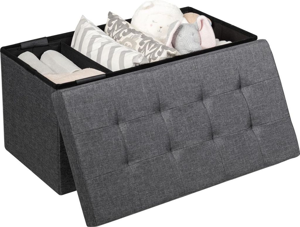 A dark gray storage ottoman with its lid open, revealing compartments filled with pillows and rolled items.