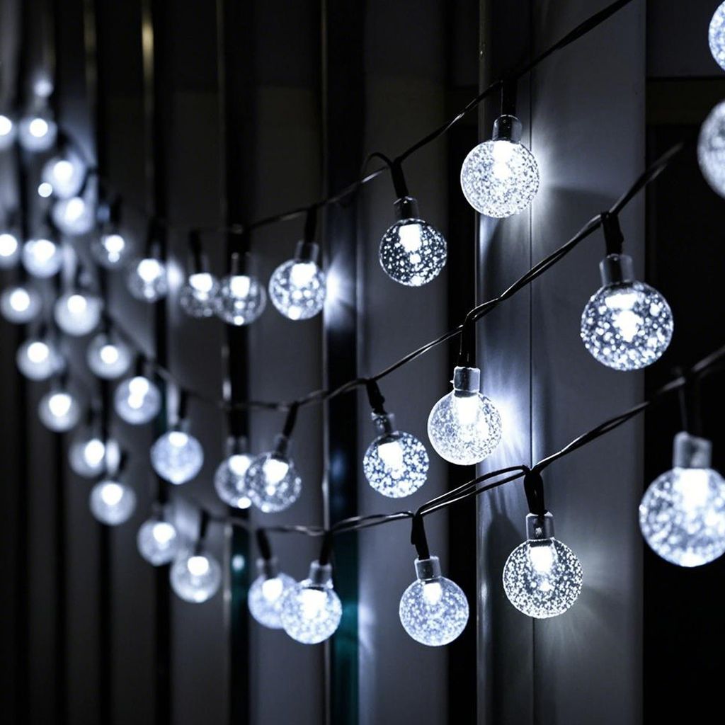 A string of solar-powered globe lights with a textured surface, hanging in front of a dark, out-of-focus background.